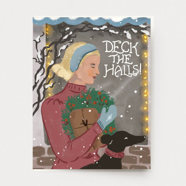 Cheerful woman and her dog holiday christmas greeting card in a vintage classic style carrying present and wreath in front of a city shop window with christmas lights and snow, illustrated by hand in california and printed in the USA